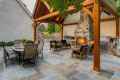 Outdoor living in Delaware County, PA shines with a stone fireplace under a wood pergola. Black-cushioned chairs encircle the fire, while a glass-top dining table invites meals. A built-in grill awaits on the right, and lush greenery envelops this expertly crafted hardscaping haven.