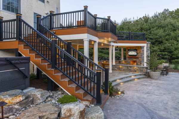 Outdoor living in Delaware County, PA shines with this multi-level patio featuring a staircase to a covered seating area. Enjoy the stone fireplace and elegant lighting fixtures, all expertly designed through our hardscaping services and surrounded by lush greenery and rocks.