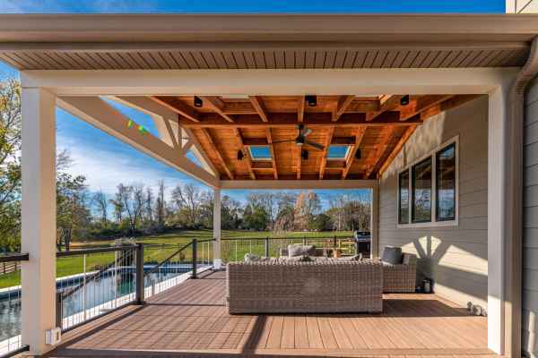 Experience outdoor living at its finest on a covered patio with a wooden ceiling and skylights. Wicker seating graces the wooden deck as you overlook the grassy yard and fenced-in pool beneath a clear blue sky. Perfect for those seeking exceptional landscaping services in Delaware County, PA.