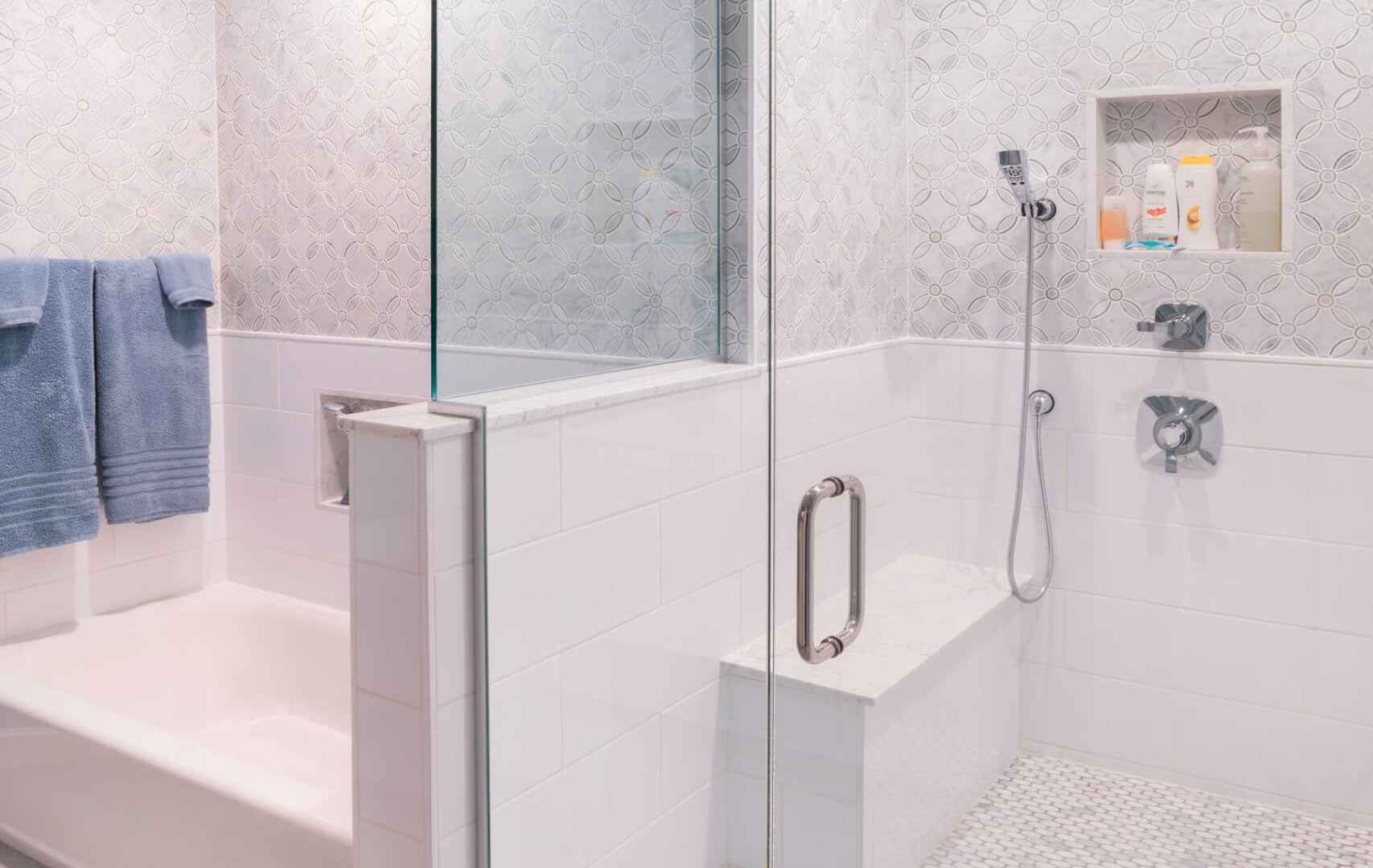 A modern bathroom features a walk-in glass shower with a built-in bench and rainfall showerhead. The walls have a textured design, and the floor has a small hexagonal tile pattern. With its seamless blend of indoor elegance and outdoor living, this space feels like an oasis.
