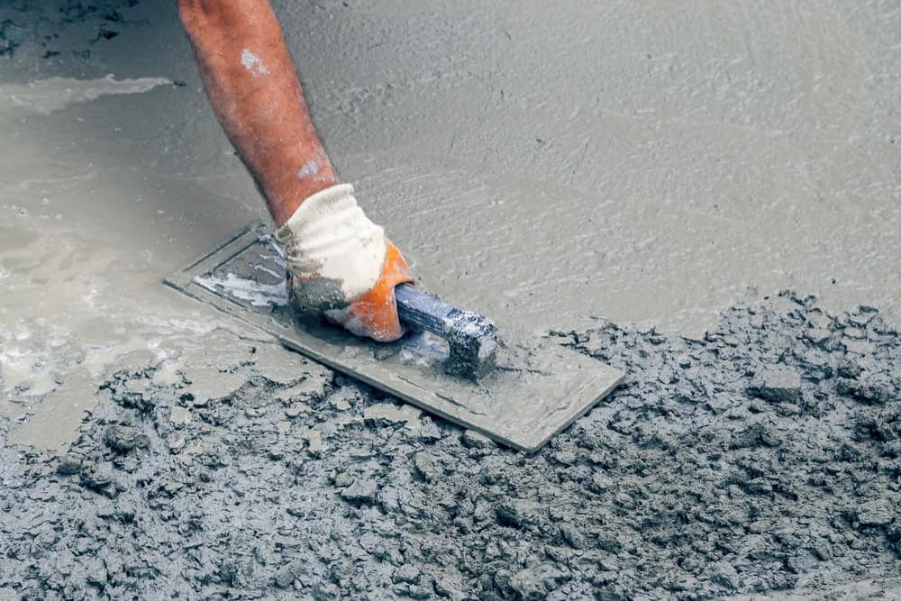 A person wearing a glove smooths wet concrete with a trowel, leveling the surface during construction work.