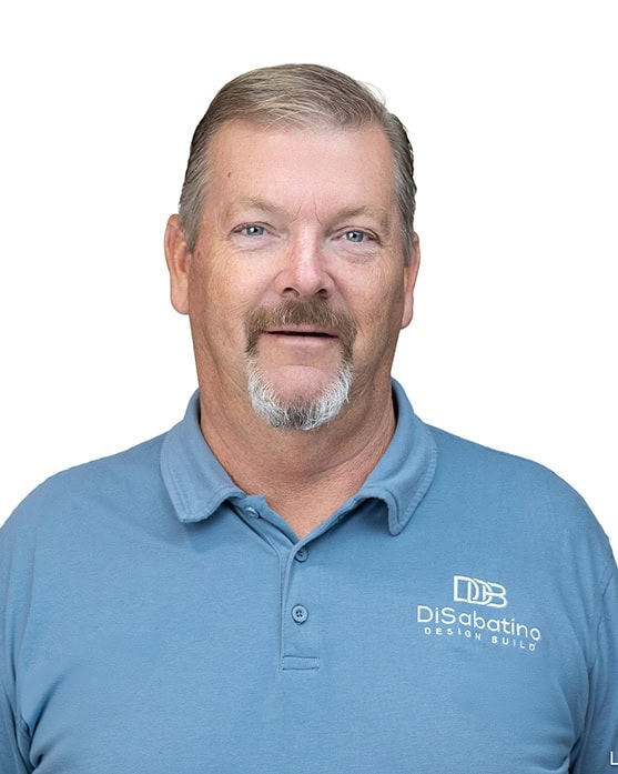 A middle-aged man with short light brown hair, a goatee, and mustache, wearing a light blue polo shirt with the "DiSabatino Design Build" logo, stands against a white background, smiling slightly.