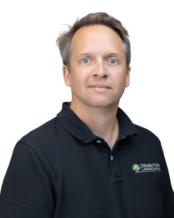 A man with short grayish hair wearing a black polo shirt with a "DiSabatino Landscaping" logo stands against a plain white background, looking directly at the camera with a neutral expression.